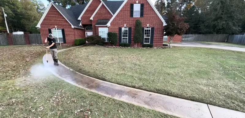 Technician pressure washing a concrete walkway in front of a brick home