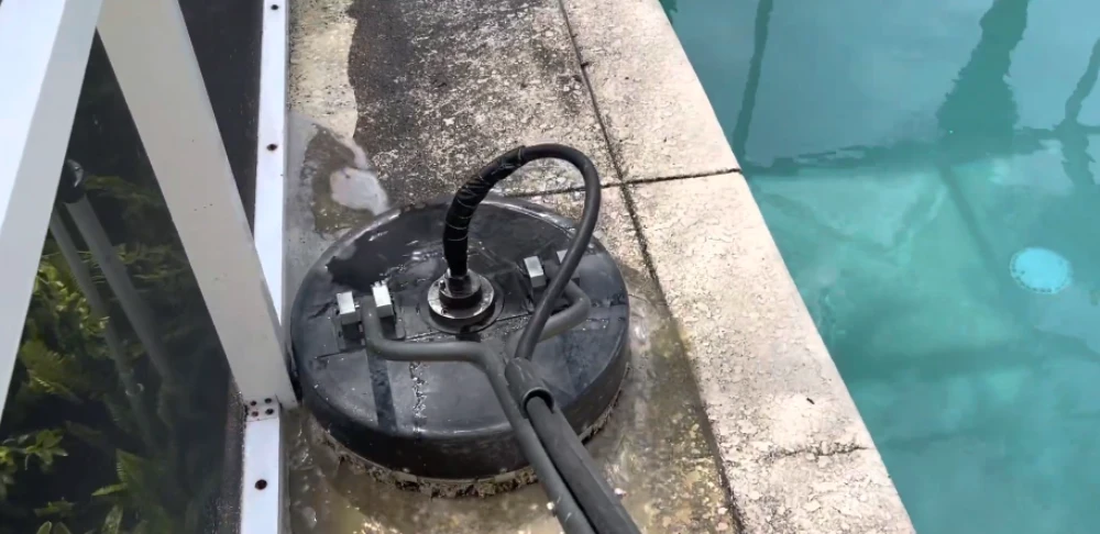 Surface cleaner removing dark algae and dirt from a concrete pool deck beside a screened pool enclosure